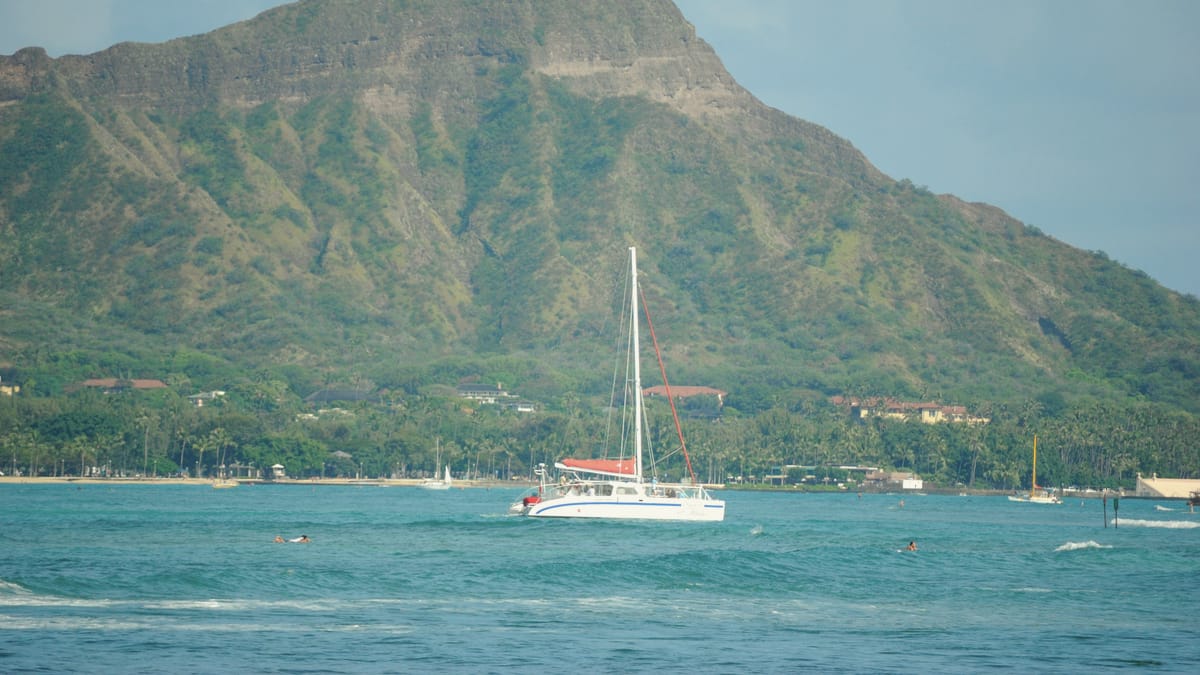 A catamaran under sail off Waikīkī, Diamond Head behind.