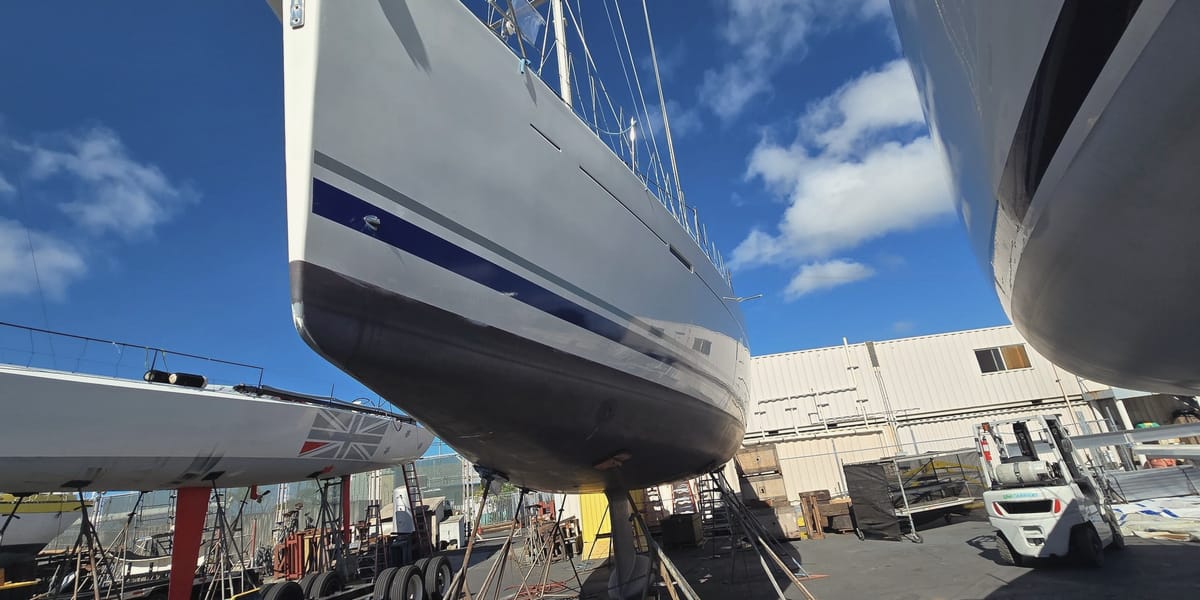 A sailboat hull up on jack stands at the Keʻehi boatyard, keel bare under a clear morning sky.
