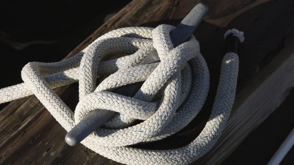 A dock line coiled and cleated off on a galvanized cleat, low sun on worn dock boards.