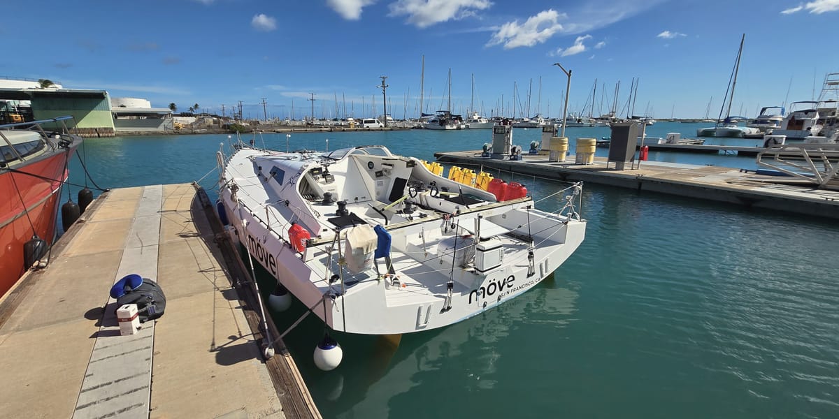 A race boat tied up at the Keʻehi Small Boat Harbor fuel dock, the mooring field and masts behind.